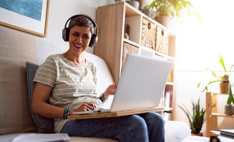 Woman wearing her headphones, smiling and working on laptop.