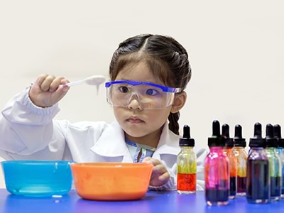 Young child dresses up as a scientist and plays with test tubes filled with colourful liquid.