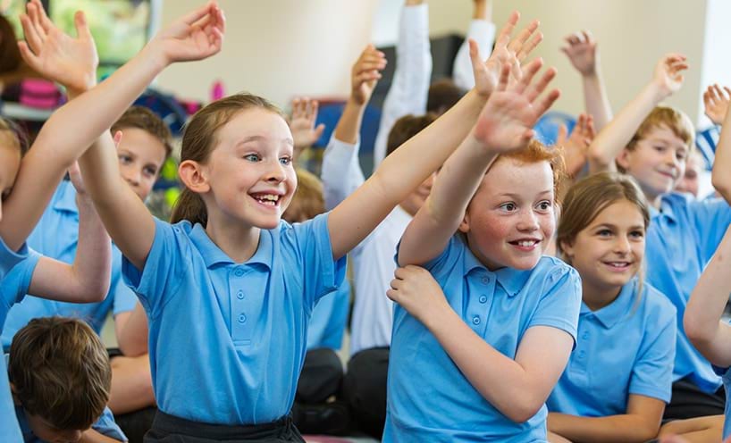 Smiling school children in uniforms with their hands up