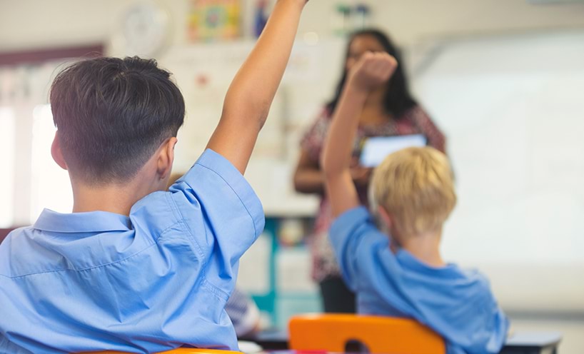 A few students raising their hands while seated in a classroom.