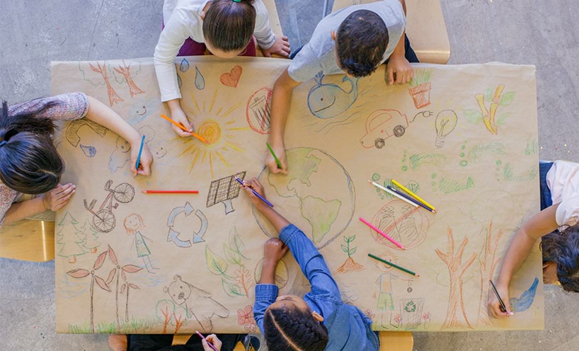 A birds eye shot of a group of students drawing sustainability images on a large brown sheet of paper.