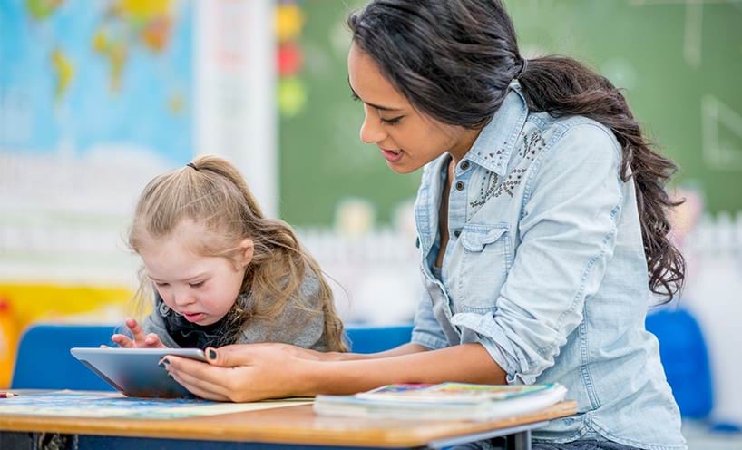 Teacher sitting with young student as they use an iPad together.