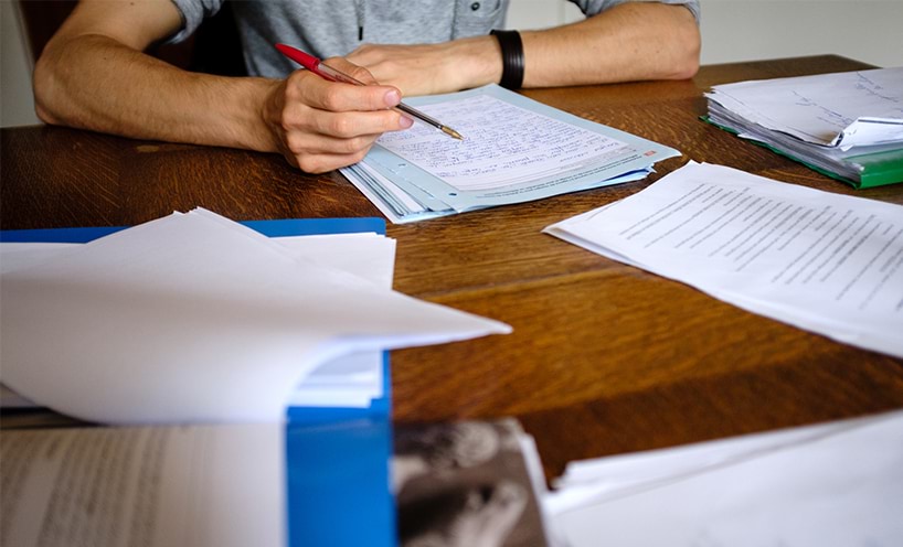 Image of a man marking multiple exam papers on a desk.