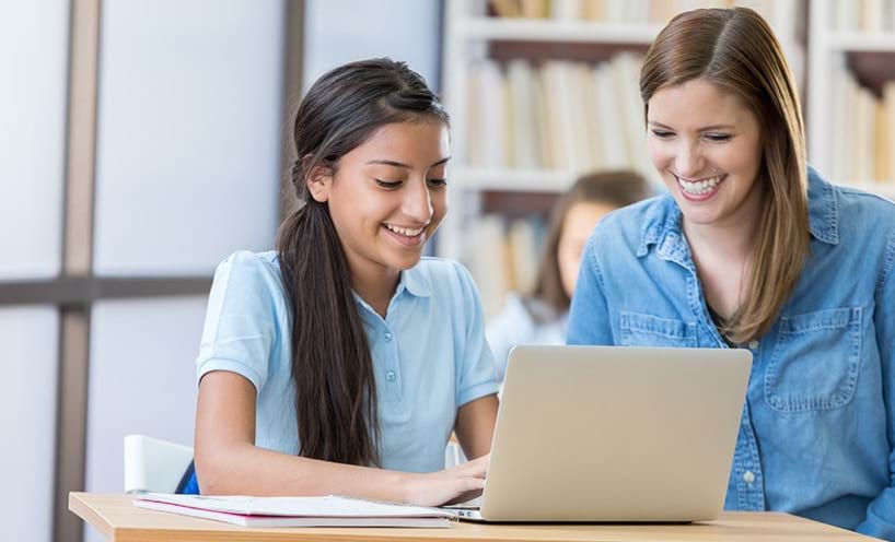 A teacher and student sit together as they work on a laptop.