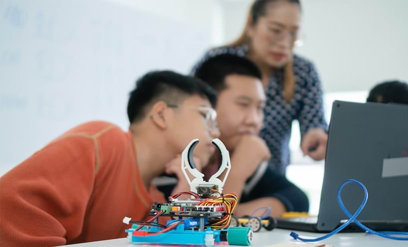 Two students learning robotics in classroom with teacher.