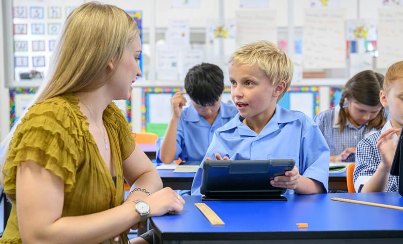 A teacher assisting a primary school-aged child a his desk. 