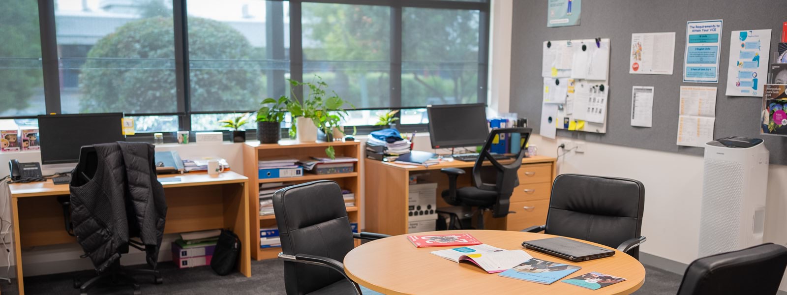 A furnished office with a table, desks, chairs and computers.