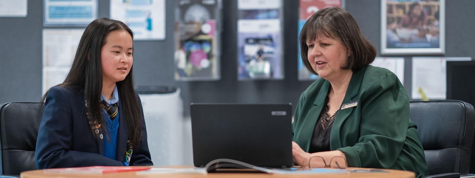 A woman and a teenage girl sit at a table with a laptop.