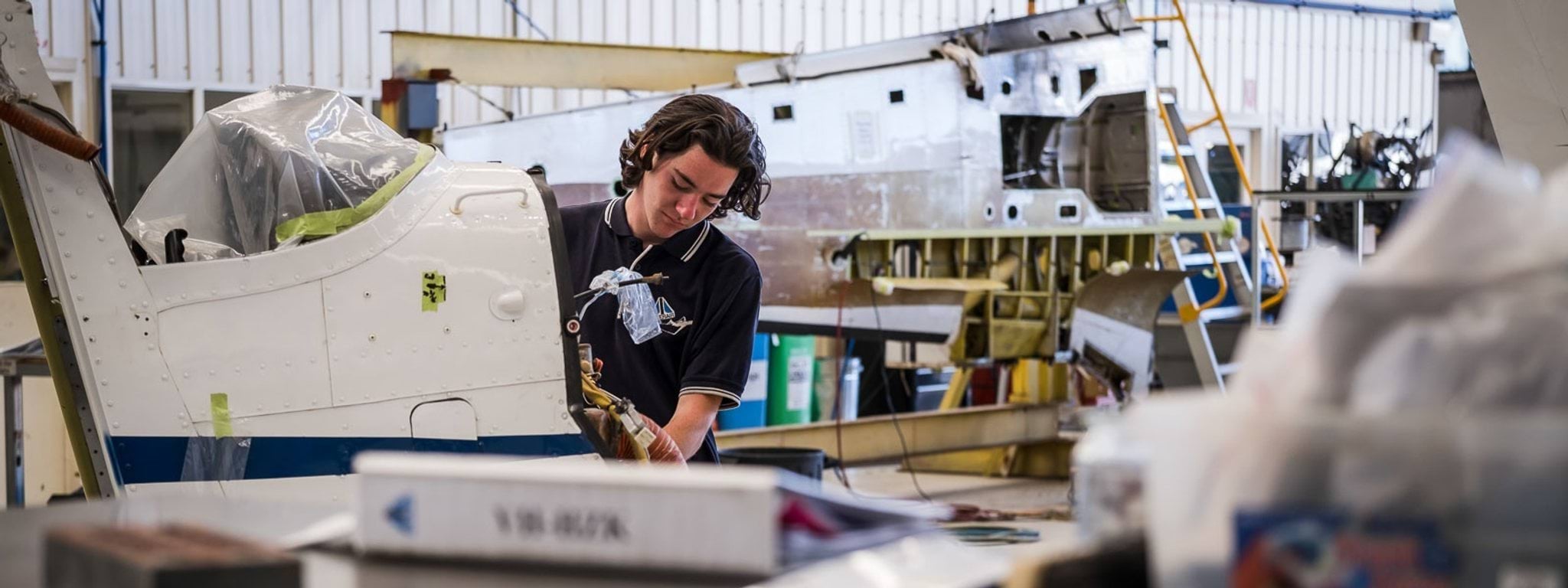 A teenage boy working on an aeroplane inside a shed.